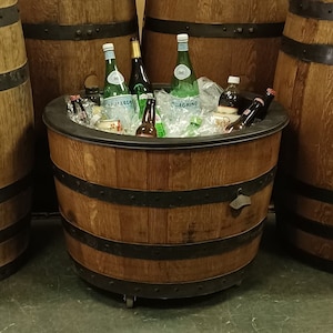 Pu&ograve; includere: Un refrigeratore a forma di barile di legno con un bordo e fasce in metallo nero. Il refrigeratore &egrave; pieno di ghiaccio e varie bottiglie di bevande, tra cui birra e acqua frizzante.