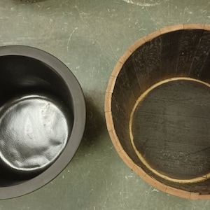 Pu&ograve; includere: Due contenitori rotondi, uno in plastica nera e uno in legno marrone, entrambi con un'apertura circolare nella parte superiore.