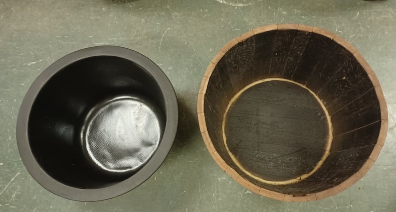 Pu&ograve; includere: Due contenitori rotondi, uno in plastica nera e uno in legno marrone, entrambi con un'apertura circolare nella parte superiore.