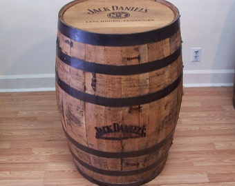 May include: A wooden Jack Daniel's whiskey barrel with black metal hoops. The barrel is used as a table and has the Jack Daniel's logo and "Lynchburg, Tennessee" printed on the top.