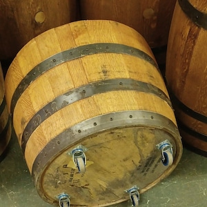 Pu&ograve; includere: Una botte di legno con fasce metalliche e quattro ruote. La botte &egrave; realizzata in legno naturale e ha un aspetto rustico. Le ruote sono in metallo e hanno un pneumatico in gomma nero.