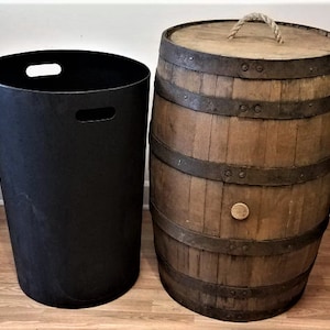 May include: A black plastic trash can with two handles sits next to a wooden barrel with metal bands and a rope handle. The barrel is brown and has a circular wooden plug in the center.