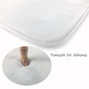 Puede incluir: Una alfombrilla de ba&ntilde;o rectangular de color blanco con una textura suave y afelpada. La imagen incluye un recuadro circular que muestra el material siendo presionado, demostrando su superficie acolchada, junto al texto Yumuşak bir dokunuş.