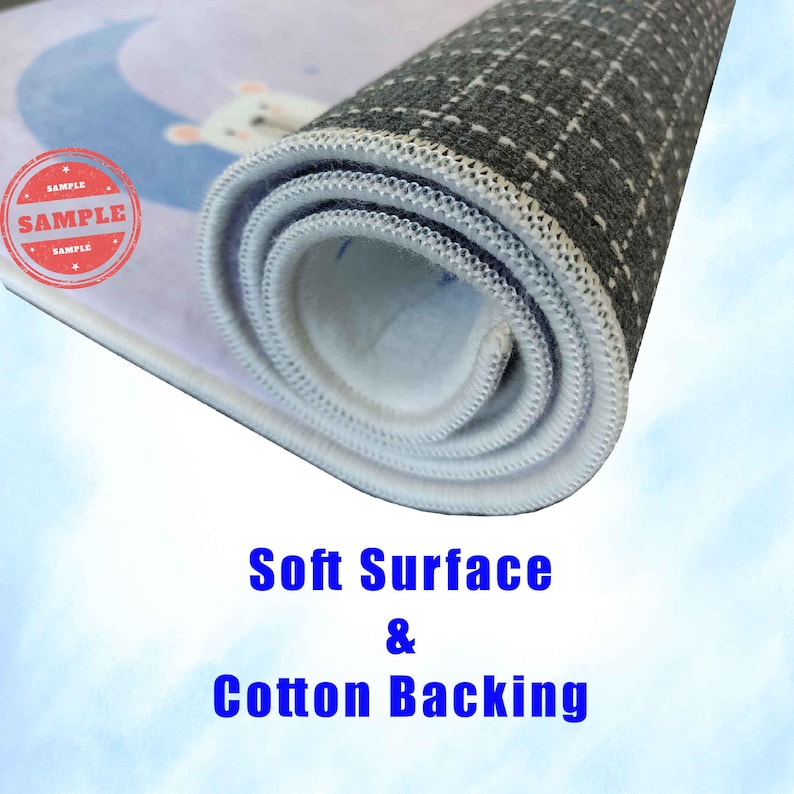 Puede incluir: Una alfombra enrollada con una superficie de color morado claro y una ilustraci&oacute;n de un oso blanco sobre una luna creciente azul. La alfombra tiene una capa superior blanca suave y un reverso gris oscuro antideslizante con rejilla blanca. Texto: Soft Surface & Cotton Backing.