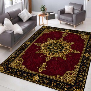 Puede incluir: Una alfombra rectangular con un centro de color rojo burdeos intenso y un gran patr&oacute;n de medall&oacute;n floral intrincado en oro y negro. La alfombra est&aacute; enmarcada por un borde negro ancho decorado con motivos florales dorados y volutas.