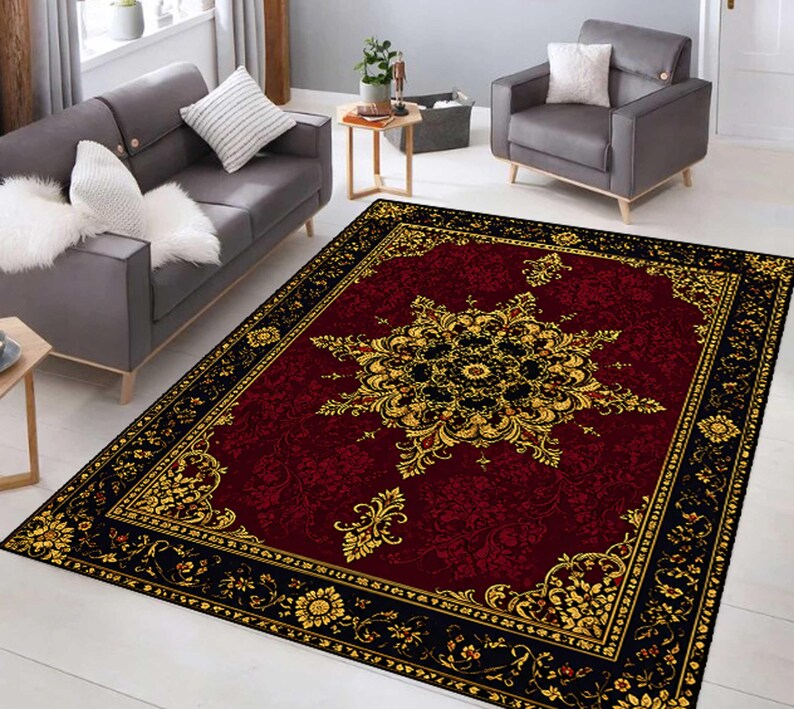 Puede incluir: Una alfombra rectangular con un centro de color rojo burdeos intenso y un gran patr&oacute;n de medall&oacute;n floral intrincado en oro y negro. La alfombra est&aacute; enmarcada por un borde negro ancho decorado con motivos florales dorados y volutas.