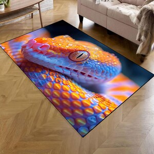 Può includere: Un tappeto rettangolare con un'immagine ravvicinata della testa di un serpente. Il serpente ha squame arancioni e blu, un naso rosa e un occhio dettagliato. Il tappeto è posto su un pavimento di legno.