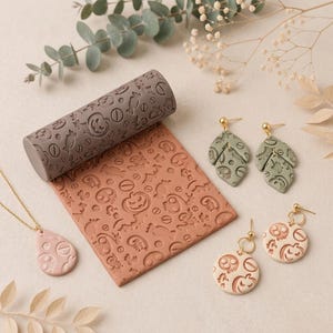 May include: A grey cylindrical texture roller and a square terracotta slab both embossed with Halloween motifs including pumpkins and sweets. Included are two sage green leaf-shaped earrings, two round cream-coloured earrings, and a pink teardrop pendant.