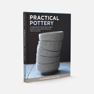May include: A book titled "Practical Pottery" with a black cover. The cover features a stack of gray ceramic bowls. The book's title and subtitle are in white text. The book is a complete guide to making bowls, plates, vases, and more.