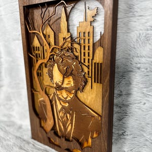 May include: A layered wooden artwork depicting a man in a suit against a cityscape with a full moon. The frame is dark brown, with the portrait and city elements in lighter shades of brown. The artwork is a unique decorative piece.