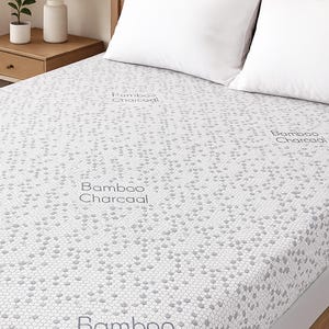 Peut inclure: Un lit avec un couvre-matelas à motifs gris clair et deux oreillers blancs. Le couvre-matelas porte l'inscription "Bamboo Charcoal". Le cadre de lit est en bois brun clair. Une lampe blanche et une petite plante sont sur la table de chevet.