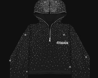 May include: Black hooded sweatshirt with a zipper and white rhinestone embellishments. The word "Studios" is written in white script on the front. The hood and sleeves are also covered in rhinestones.