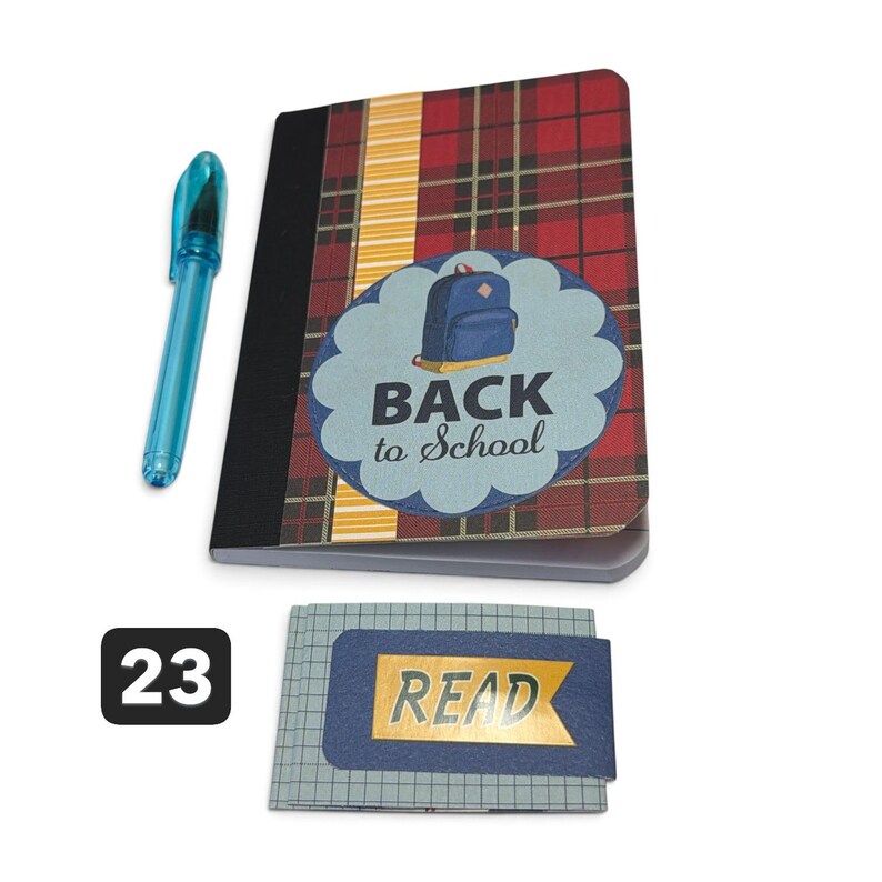 May include: A red and black plaid notebook with a blue scalloped sticker featuring a backpack and the text BACK to School, a translucent blue pen, and a small grid-patterned notepad with a blue banner sticker displaying the word READ.