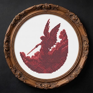 May include: A framed cross-stitch artwork depicting a red angel figure with a sword, rising from a cloud-like shape. The artwork is set within an ornate, oval wooden frame. The background is a solid black.