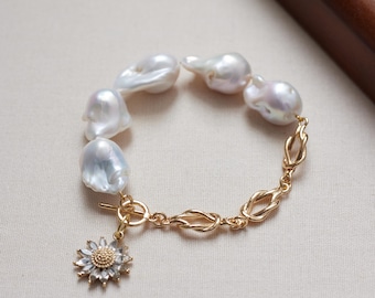 Puede incluir: Una pulsera con cinco perlas barrocas blancas irregulares y una cadena de metal dorado con eslabones trenzados. La pieza incluye un cierre de barra y un dije en forma de girasol con pétalos de cristal transparente y un centro texturizado.