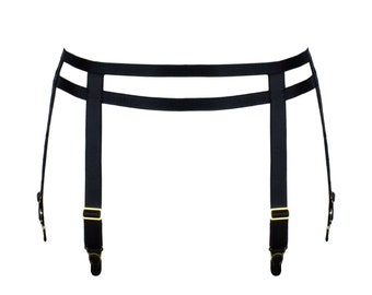 Könnte beinhalten: Schwarzer Strumpfhalter mit zwei horizontalen Bändern und vier vertikalen Trägern. Die Träger haben goldfarbene Metallbeschläge und verstellbare Verschlüsse. Der Strumpfhalter ist für das Tragen um die Taille konzipiert.