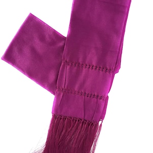 May include: A vibrant magenta scarf with a rectangular shape. The scarf features decorative cut-out patterns and a fringe at the bottom. The fabric appears to be a smooth, silky material.
