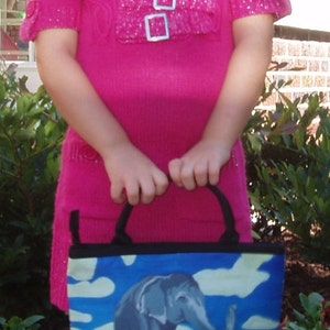 May include: A young girl wearing a pink sweater with a sparkly design and black and white floral leggings is holding a blue and white tote bag with a painted image of an elephant and a baby elephant.