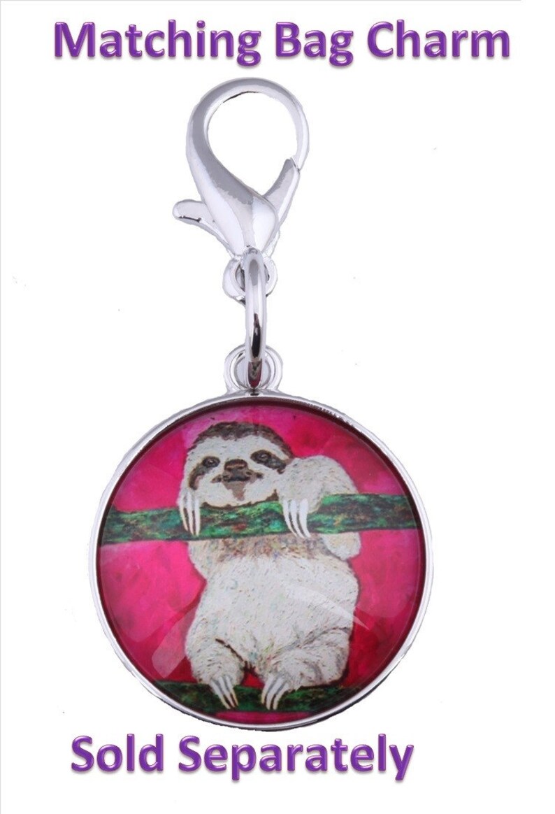 May include: A silver bag charm with a round, pink and green glass charm featuring a sloth hanging from a branch. The charm has a silver clasp.