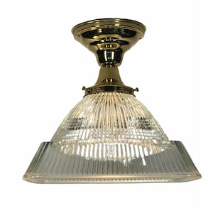 May include: A vintage-style ceiling light fixture with a brass finish. The light has a clear, ribbed glass shade in a conical shape, and a brass base. The fixture is designed for ceiling mounting and provides ambient lighting.