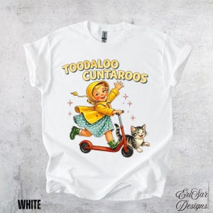 May include: White t-shirt featuring a vintage illustration of a girl riding a red scooter with a gray tabby cat. The girl wears a yellow raincoat and a blue dress. The text "TOODALOO CUNTAROOS" is printed above the illustration.