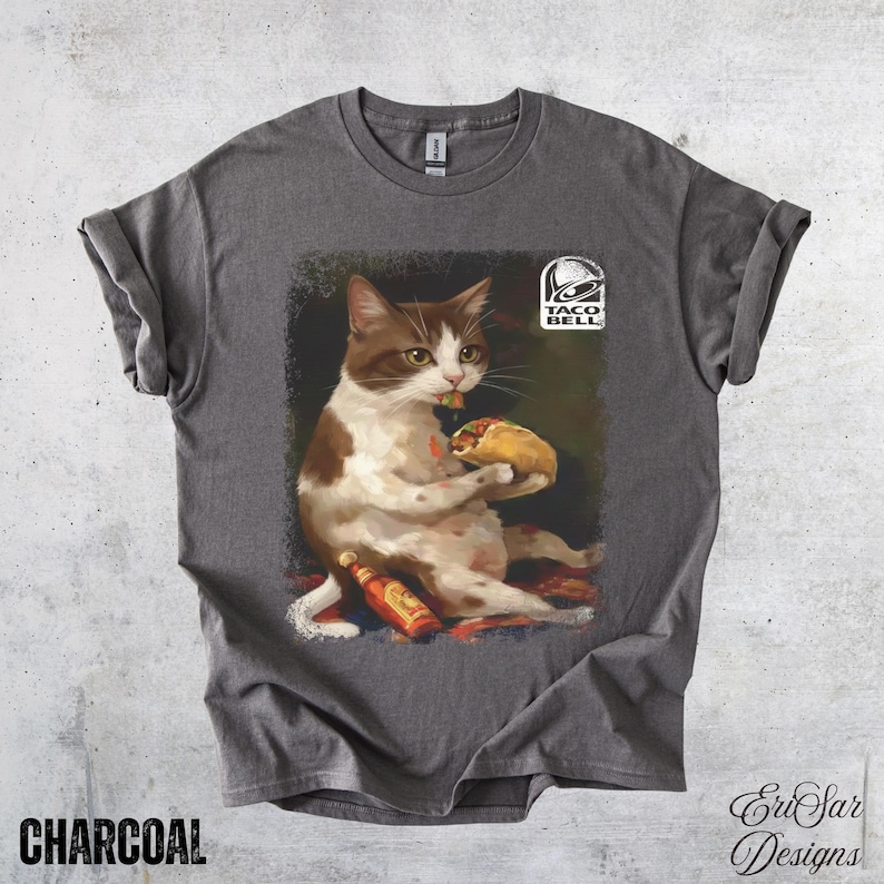 May include: Charcoal-colored t-shirt featuring a whimsical illustration of a cat enjoying a taco, with a Taco Bell logo. The cat is brown and white, holding a taco and a bottle of hot sauce. The text "CHARCOAL" is at the bottom.