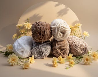 May include: A selection of yarn balls in white, brown, and grey, arranged in a pile. Yellow flowers are scattered around the yarn, with a soft, neutral background. Suitable for knitting and crochet projects.