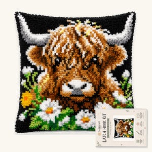 Peut inclure: Un kit de crochet à loquet carré représentant une vache Highland avec de longues cornes et une fourrure brune hirsute sur fond noir, entourée de fleurs blanches et jaunes. Le kit inclut une carte d'instructions avec le texte LATCH HOOK KIT.