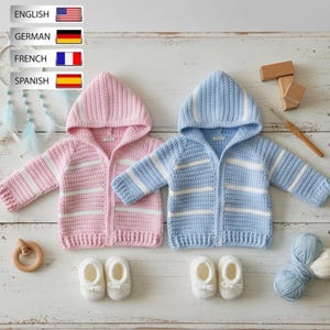 以下が含まれることがあります： 手作りのベビー用フード付きセーター2着。ピンクと水色で、それぞれ白いストライプが入っています。白いベビーブーティーも写っています。木製のおもちゃと糸も写っており、手芸がテーマであることがわかります。