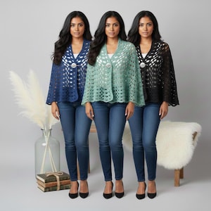 May include: Three women modelling open-weave crochet capes in navy, seafoam green, and black. Each cape is fastened with a decorative button. They are paired with blue jeans and black heels. The capes have a delicate, lacy appearance.