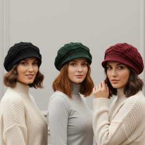 May include: Three women wearing knitted beret hats in black, green, and burgundy. The hats have a textured design and are paired with neutral-colored turtleneck sweaters. The background is a plain, light gray.
