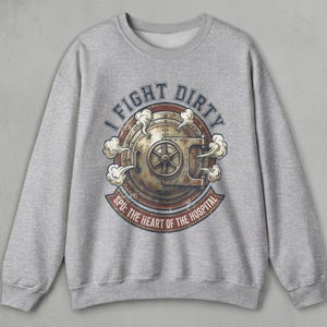 May include: A grey sweatshirt with a distressed graphic. The graphic features a circular design with the text "I FIGHT DIRTY" and "SPD: THE HEART OF THE HOSPITAL". The design includes a rusty metal door with a wheel and steam.