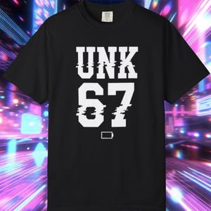 May include: Black t-shirt with the white text "UNK 67" in a glitch effect font. A small battery icon is below the number 67. The shirt has a crew neck and short sleeves.
