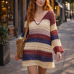 May include: A striped crochet dress with a V-neck in shades of cream, burgundy, blue, and lavender. The long-sleeved dress has a loose, relaxed fit. A brown suede shoulder bag is also visible.