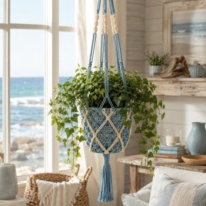 May include: A macrame plant hanger crafted from light blue and cream-coloured cord, featuring a diamond-patterned net design that holds a lush green ivy plant. The hanger includes a long, solid light blue tassel at the bottom and braided cords.