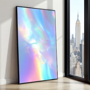 Puede incluir: Una impresión artística enmarcada con un diseño abstracto de colores iridiscentes, incluyendo tonos de azul, morado y amarillo. La obra de arte se muestra en un marco negro y se apoya en una pared blanca. En el fondo se ve una vista de la ciudad.