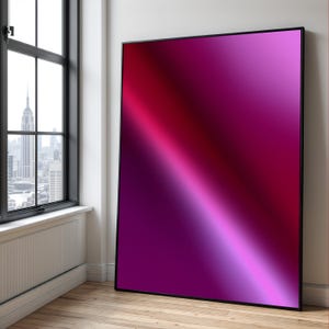 Puede incluir: Una gran obra de arte enmarcada con un degradado de colores que va del rojo intenso al rosa claro y al morado. La obra de arte está apoyada contra una pared blanca sobre un suelo de madera, junto a una ventana con vistas a la ciudad.