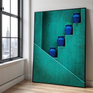 May include: A framed art print featuring a teal-colored wall with a staircase design. Four cobalt blue ceramic pots are arranged on the steps. The artwork is displayed in a room with a window overlooking a cityscape.