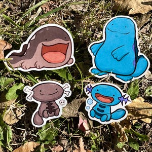 May include: Four colorful cartoon stickers featuring aquatic creatures. One is brown with a large open mouth, another is blue with a smiling face, and two are brown and blue axolotl-like creatures with skeleton designs.