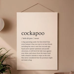 Peut inclure: Une affiche murale rectangulaire sur fond beige clair présentant le mot cockapoo en texte noir, suivi de sa prononciation phonétique, de sa classification en tant que nom et d'un paragraphe descriptif humoristique sur la race.