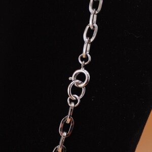 Op de afbeelding: Een zilverkleurige ketting met ovale schakels en een karabijnsluiting. De ketting wordt getoond tegen een zwarte achtergrond, wat de metallic glans en het eenvoudige ontwerp benadrukt. De ketting is een klassiek sieraad.
