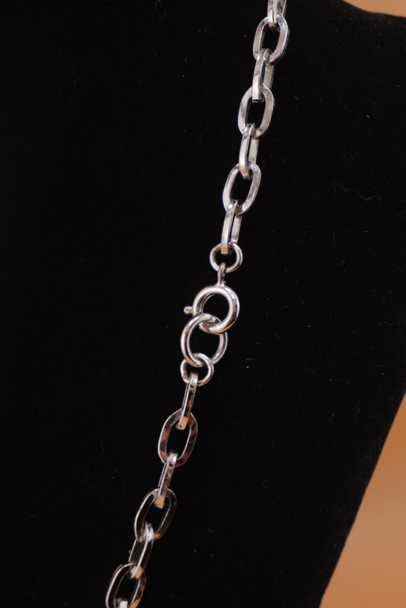Op de afbeelding: Een zilverkleurige ketting met ovale schakels en een karabijnsluiting. De ketting wordt getoond tegen een zwarte achtergrond, wat de metallic glans en het eenvoudige ontwerp benadrukt. De ketting is een klassiek sieraad.
