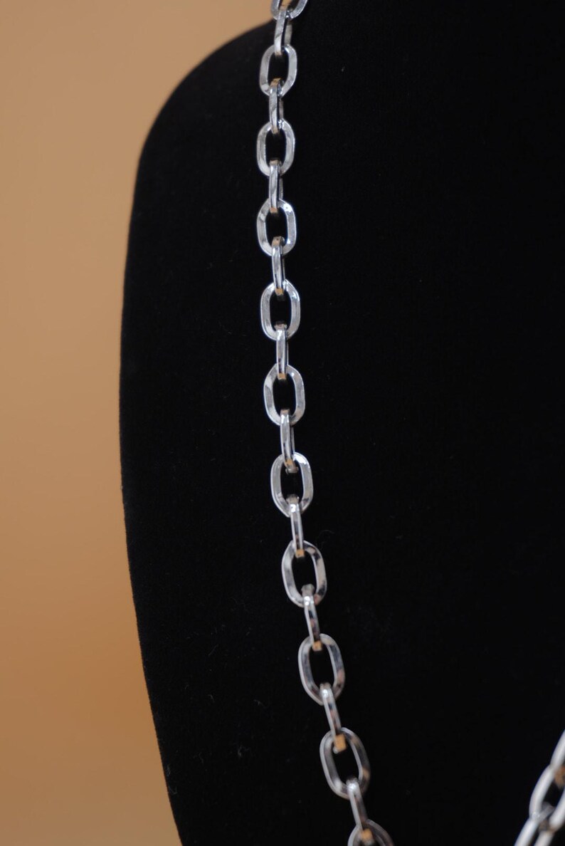 Op de afbeelding: Een zilverkleurige ketting met grote ovale schakels. De ketting wordt gepresenteerd tegen een zwarte achtergrond, waardoor het reflecterende oppervlak wordt benadrukt. De ketting is een eenvoudig maar elegant sieraad.