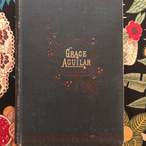 May include: A dark blue book with gold lettering on the cover. The title is "GRACE AGUILAR" and is surrounded by a decorative border.