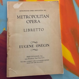 May include: A vintage libretto for the Metropolitan Opera's production of Eugene Onegin. The cover is a faded beige with black text, including the opera title and the publisher's information from Fred Rullman, Inc., New York.