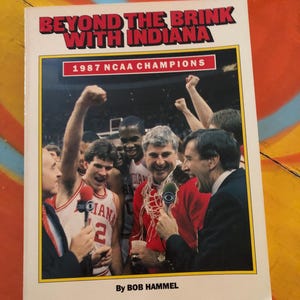 May include: A book titled "Beyond the Brink with Indiana" featuring a photo of a basketball team celebrating. The cover includes the text "1987 NCAA Champions" and is authored by Bob Hammel.