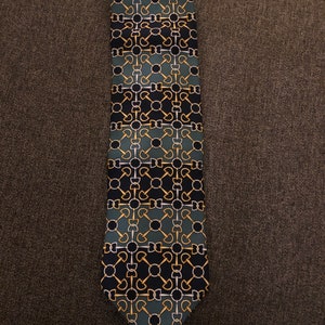May include: A dark blue and green patterned tie with a geometric design. The pattern features gold and silver accents.