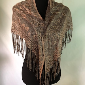 May include: A brown and gold shawl with a floral lace pattern and fringe. The shawl is draped over a black mannequin, showcasing its intricate design and texture. The color palette includes shades of brown and gold.