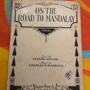 May include: Vintage sheet music cover for "On The Road To Mandalay" with text in black. The cover features decorative borders and the names of Rudyard Kipling and Charles H. Maskell. Published by Morris Music Co.