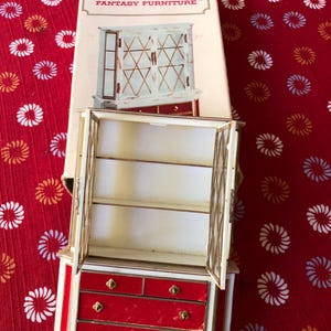 May include: A Petite Princess Fantasy Furniture miniature cabinet with red drawers and a white and gold frame. The cabinet doors are open, revealing shelves. The box is visible in the background.